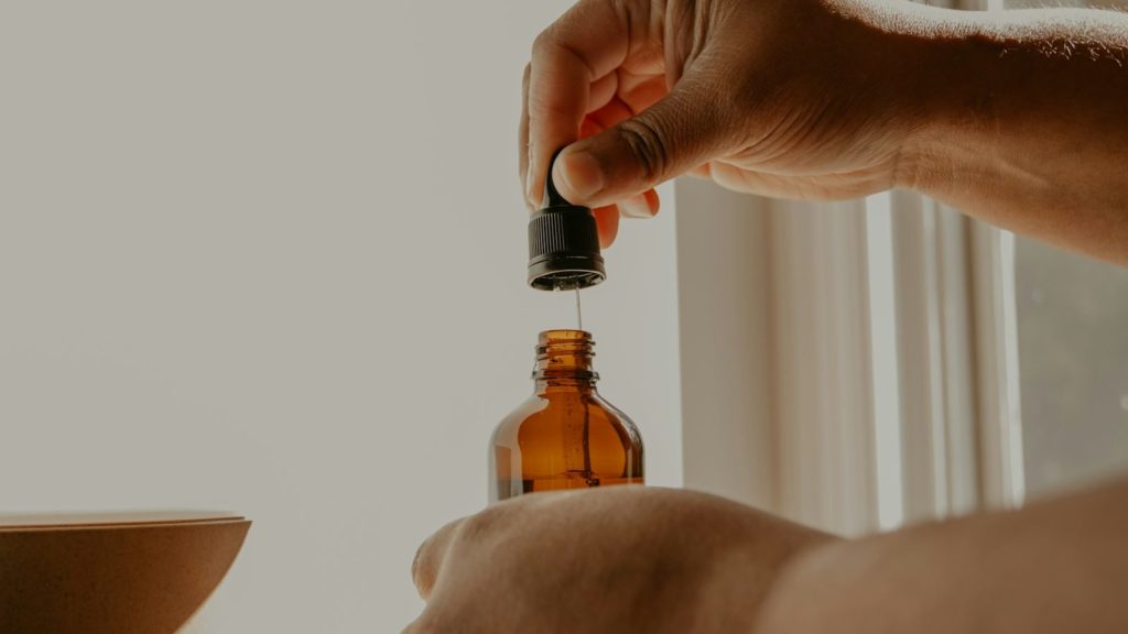 person holding brown glass bottle, huiles essentielles plexus solaire