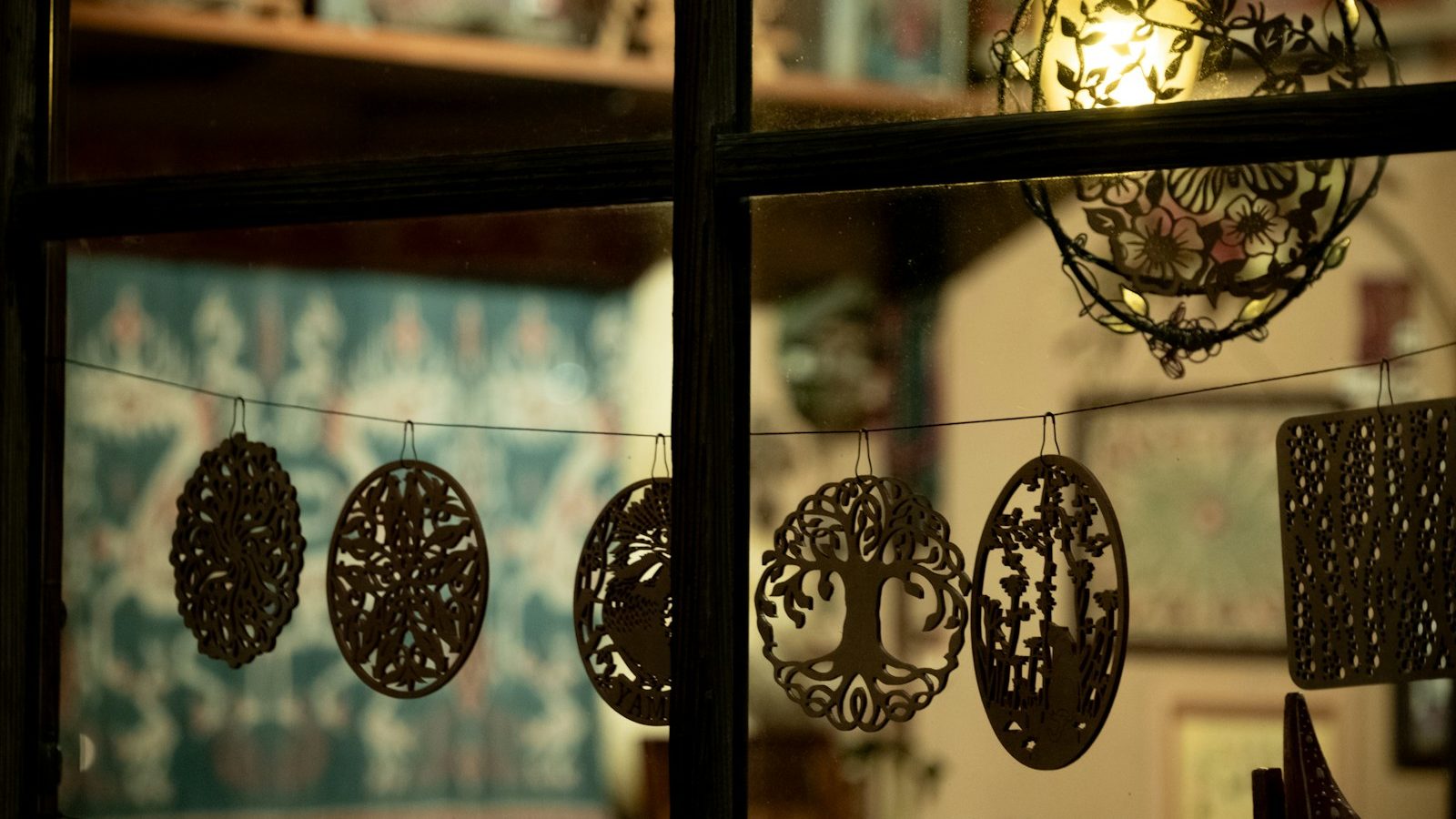 Ornate cutouts hang on a string in a window.